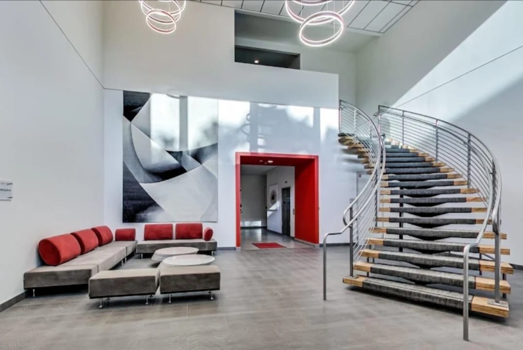 Sola Pavilion building lobby featuring a curved staircase, red accent doorway, and modern lounge seating